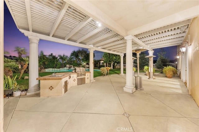 patio terrace at dusk featuring an outdoor kitchen, area for grilling, and sink