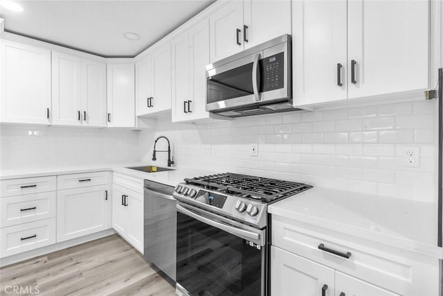 kitchen with sink, light hardwood / wood-style flooring, backsplash, white cabinets, and appliances with stainless steel finishes