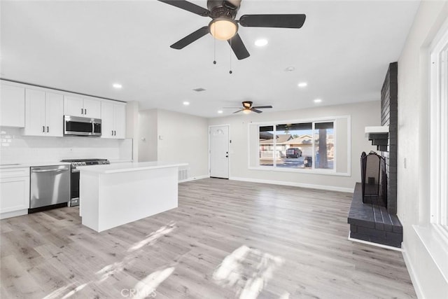 kitchen with appliances with stainless steel finishes, ceiling fan, white cabinets, light hardwood / wood-style floors, and a kitchen island