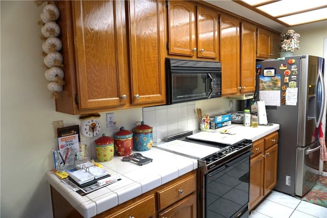 kitchen with tasteful backsplash, tile counters, light tile patterned floors, and black appliances