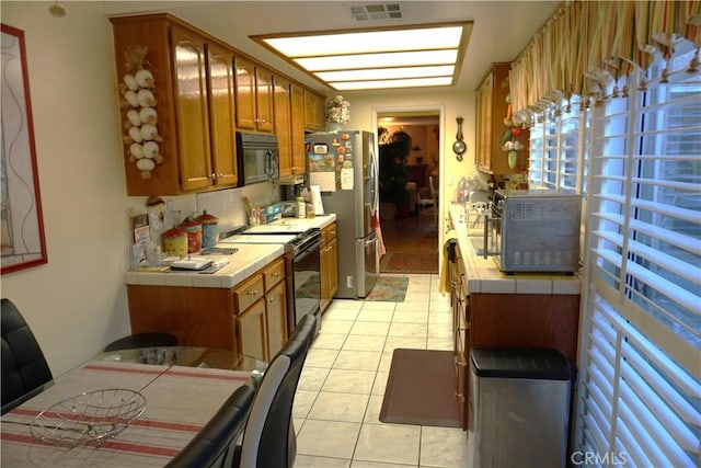 kitchen with tile countertops, light tile patterned floors, and stainless steel appliances