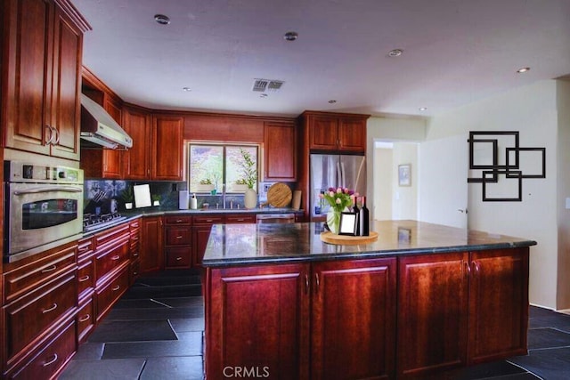 kitchen featuring decorative backsplash, appliances with stainless steel finishes, exhaust hood, dark stone countertops, and a kitchen island