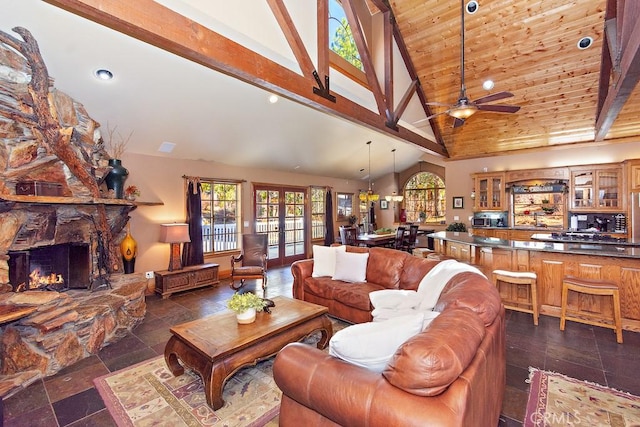 living room featuring beam ceiling, a stone fireplace, ceiling fan, and high vaulted ceiling