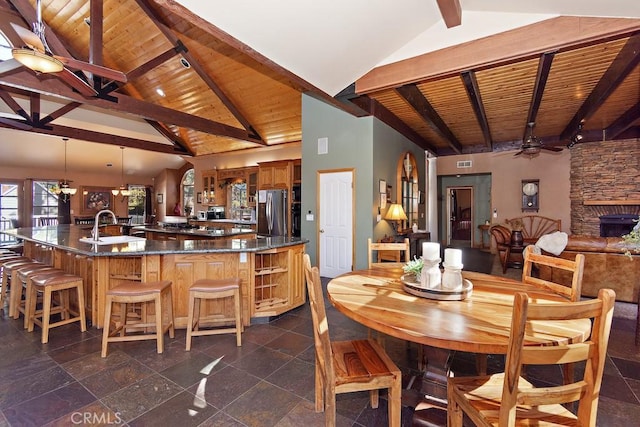 dining room with a stone fireplace, sink, ceiling fan, beamed ceiling, and wood ceiling