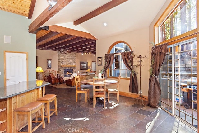 dining area with ceiling fan, lofted ceiling with beams, and a stone fireplace