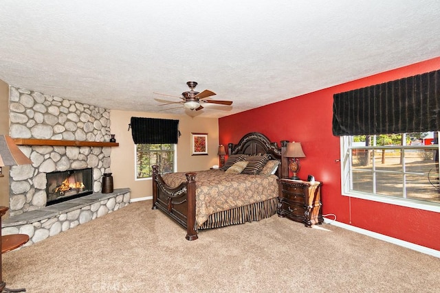 bedroom with a stone fireplace, ceiling fan, carpet floors, and a textured ceiling