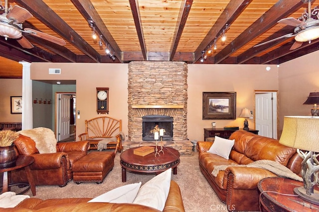 living room featuring beam ceiling, a stone fireplace, ceiling fan, and light colored carpet