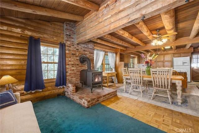 interior space with a wood stove, plenty of natural light, wooden ceiling, and ceiling fan