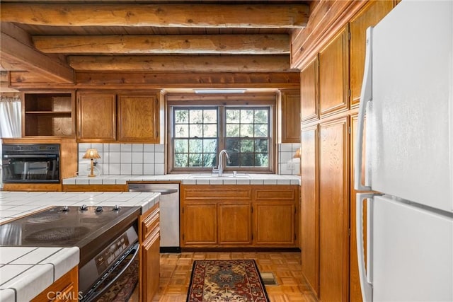 kitchen featuring decorative backsplash, sink, black appliances, beamed ceiling, and tile counters