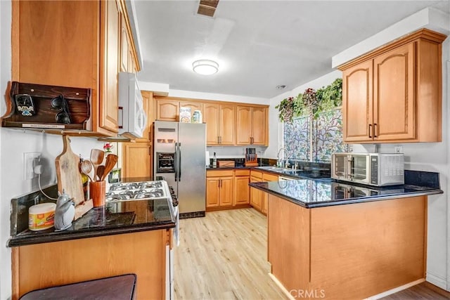 kitchen with sink, light hardwood / wood-style flooring, dark stone countertops, kitchen peninsula, and stainless steel appliances