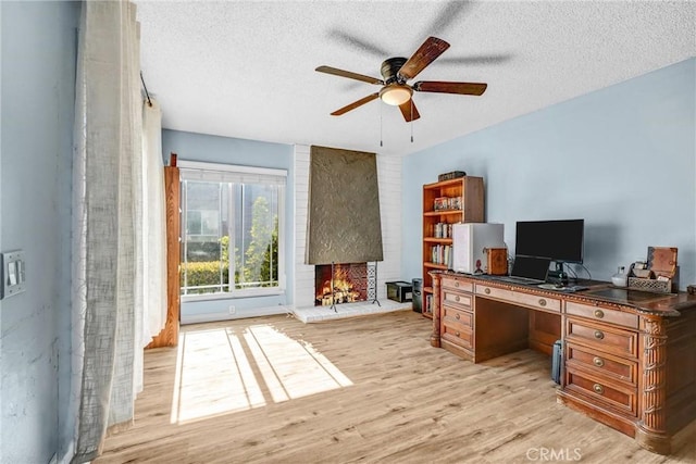 office space featuring ceiling fan, light hardwood / wood-style flooring, a textured ceiling, and a brick fireplace