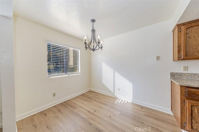 unfurnished dining area with a notable chandelier and light wood-type flooring