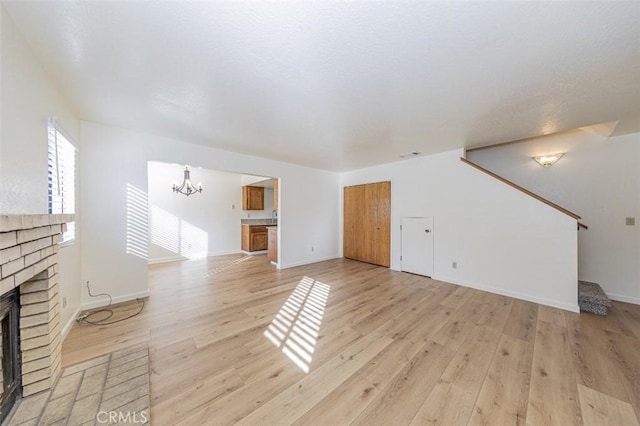 unfurnished living room with a fireplace, a chandelier, and light hardwood / wood-style flooring