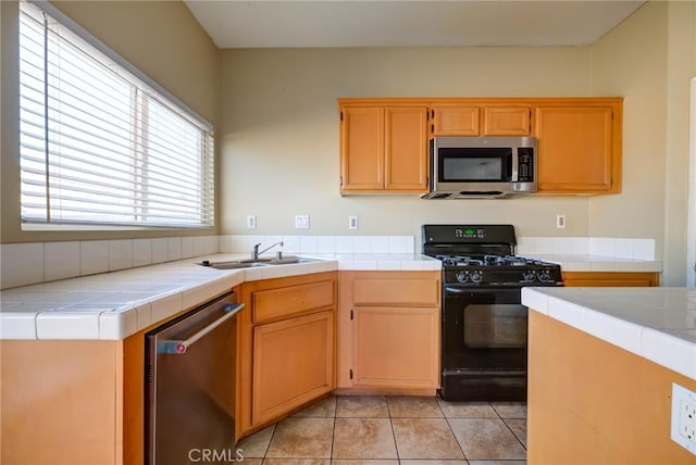 kitchen featuring tile countertops, sink, light tile patterned floors, and appliances with stainless steel finishes