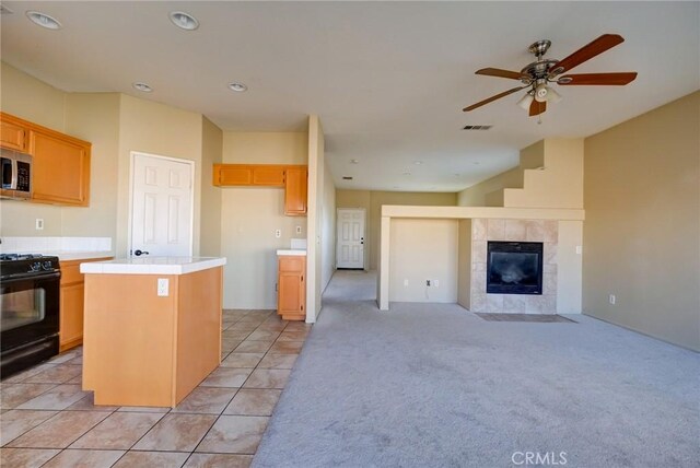 kitchen featuring light brown cabinetry, black range oven, ceiling fan, a center island, and a tiled fireplace