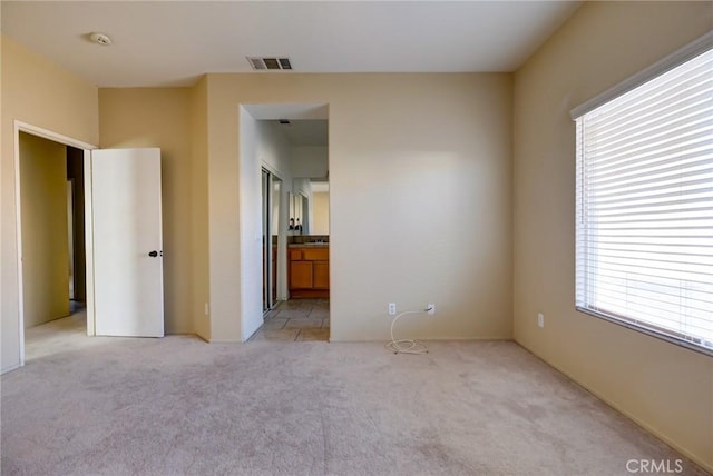 unfurnished bedroom featuring connected bathroom, light carpet, and multiple windows