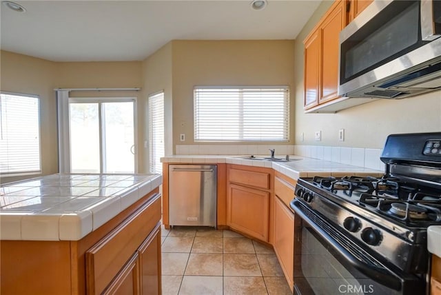 kitchen featuring light tile patterned floors, stainless steel appliances, tile counters, and sink