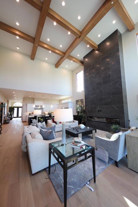 living room featuring coffered ceiling, light wood-type flooring, a towering ceiling, beamed ceiling, and a tiled fireplace