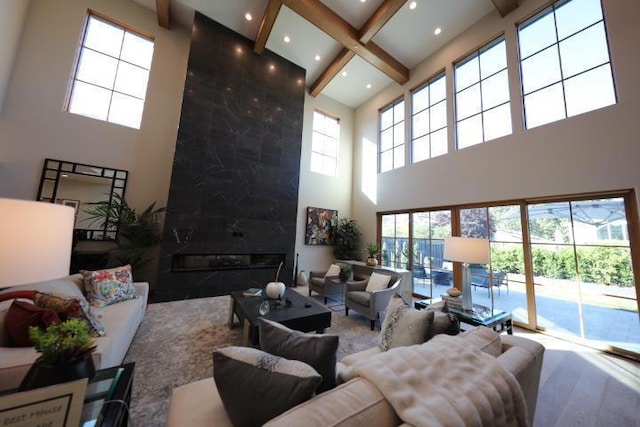 living room with beamed ceiling, a high ceiling, a healthy amount of sunlight, and a high end fireplace