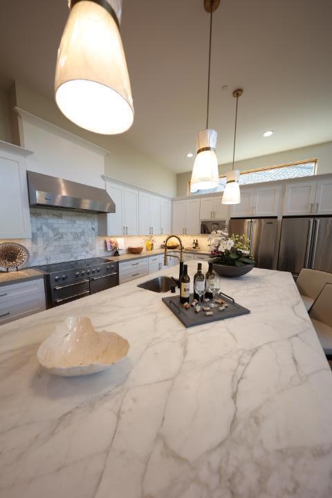 kitchen with decorative backsplash, stainless steel fridge, light stone countertops, wall chimney exhaust hood, and sink