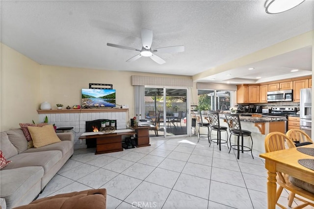 tiled living room with ceiling fan, a textured ceiling, and a brick fireplace