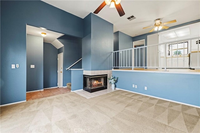 unfurnished living room featuring a tiled fireplace, light carpet, and ceiling fan