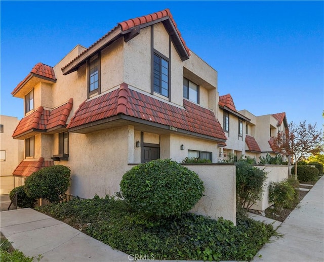 view of side of home featuring stucco siding, a tiled roof, and fence