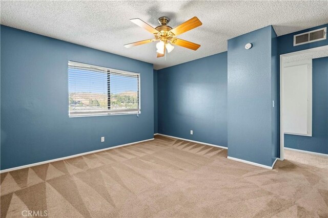 empty room featuring a textured ceiling, light colored carpet, and ceiling fan