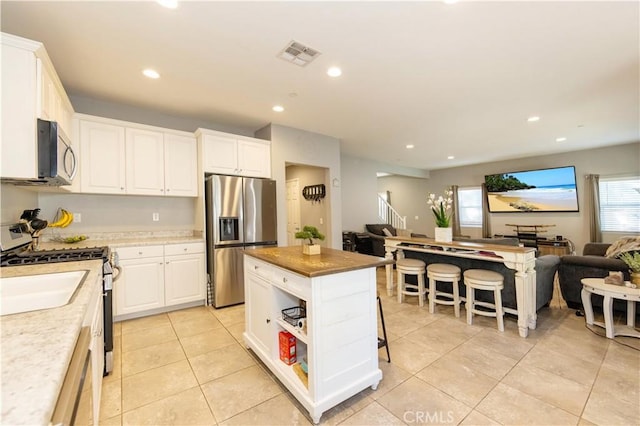 kitchen with white cabinetry, a center island, stainless steel appliances, a breakfast bar area, and light tile patterned floors