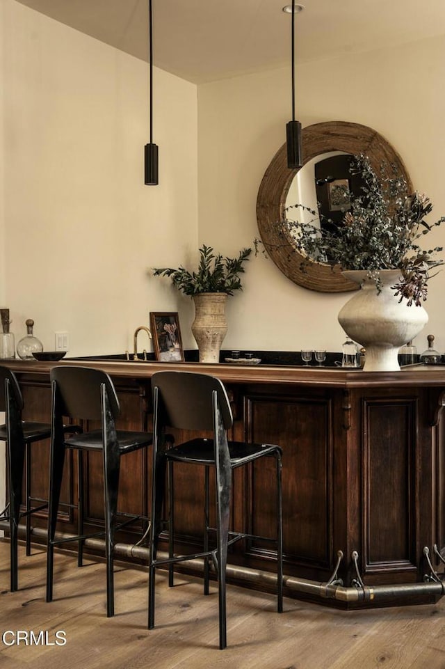 bar featuring dark brown cabinets, light wood-type flooring, and hanging light fixtures