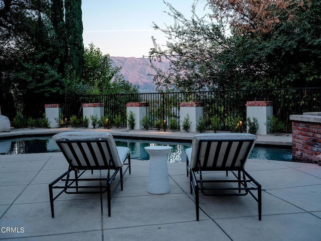 patio terrace at dusk with a mountain view and a fenced in pool