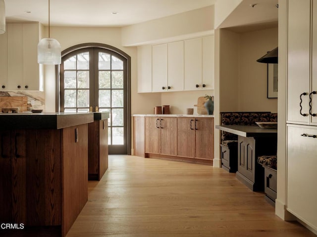 kitchen featuring light wood-type flooring, white cabinetry, hanging light fixtures, and backsplash