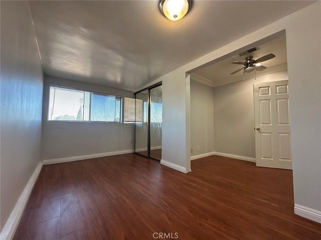 empty room with ceiling fan, crown molding, and dark wood-type flooring