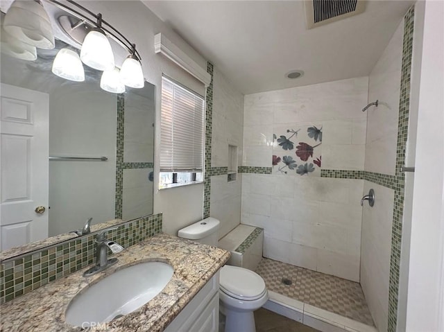 bathroom with a tile shower, decorative backsplash, vanity, and toilet