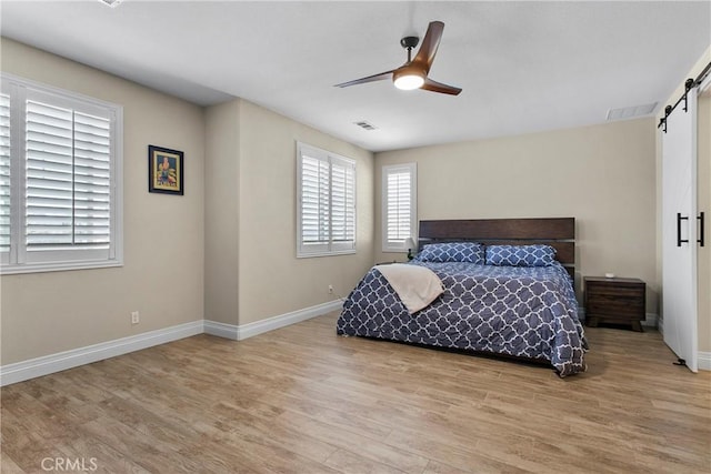 bedroom featuring light wood-type flooring, ceiling fan, and a barn door