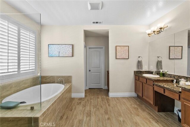 bathroom with hardwood / wood-style flooring, a relaxing tiled tub, and vanity