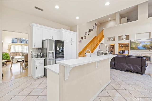 kitchen featuring a breakfast bar, white cabinets, a center island with sink, light tile patterned flooring, and stainless steel fridge with ice dispenser