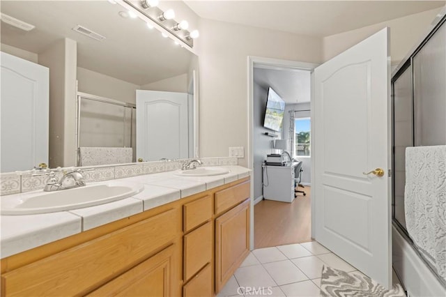 bathroom with tile patterned flooring, vanity, and bath / shower combo with glass door