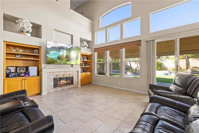 living room with built in shelves, light tile patterned floors, a towering ceiling, and a tile fireplace