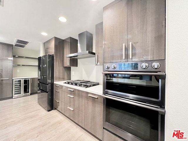 kitchen with light hardwood / wood-style flooring, beverage cooler, wall chimney range hood, and appliances with stainless steel finishes