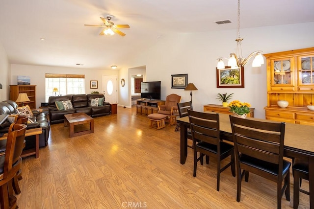 dining area featuring ceiling fan with notable chandelier, vaulted ceiling, and light wood-type flooring