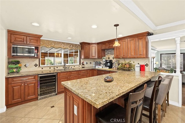 kitchen featuring a kitchen breakfast bar, light stone counters, sink, decorative light fixtures, and wine cooler