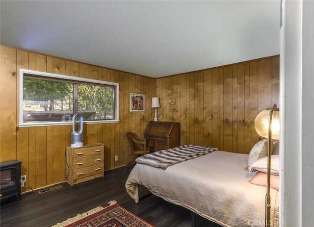 bedroom featuring a wood stove, wooden walls, and dark wood-type flooring