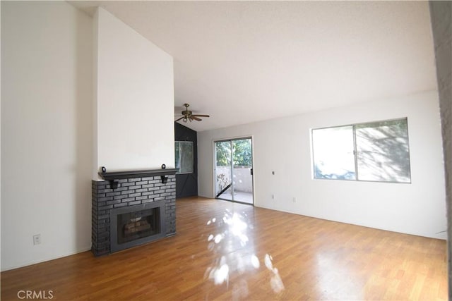 unfurnished living room featuring ceiling fan, lofted ceiling, a brick fireplace, and wood finished floors