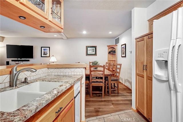 kitchen with light tile patterned floors, sink, white refrigerator with ice dispenser, and light stone counters