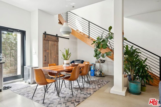 dining room with a towering ceiling, a barn door, and concrete flooring