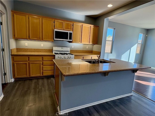 kitchen featuring sink, dark hardwood / wood-style floors, white gas range, an island with sink, and a breakfast bar area