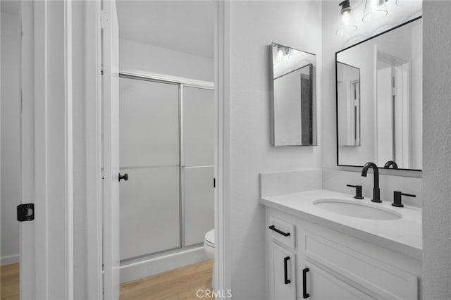 bathroom with toilet, vanity, a shower with shower door, and hardwood / wood-style flooring