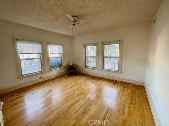 empty room with ceiling fan, a healthy amount of sunlight, a textured ceiling, and light wood-type flooring