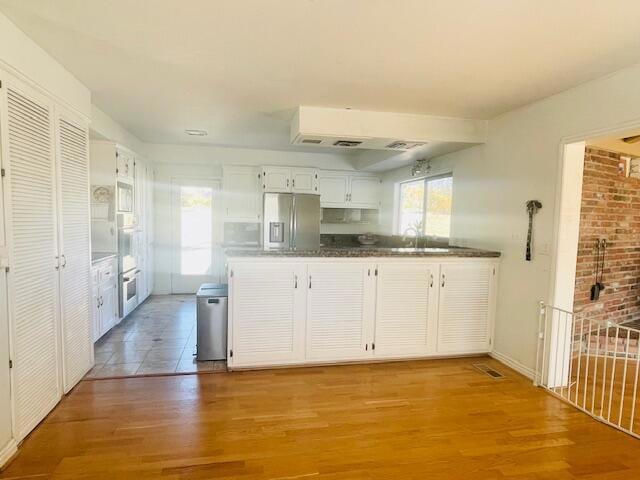 kitchen featuring white cabinetry, light hardwood / wood-style floors, kitchen peninsula, stainless steel refrigerator with ice dispenser, and oven